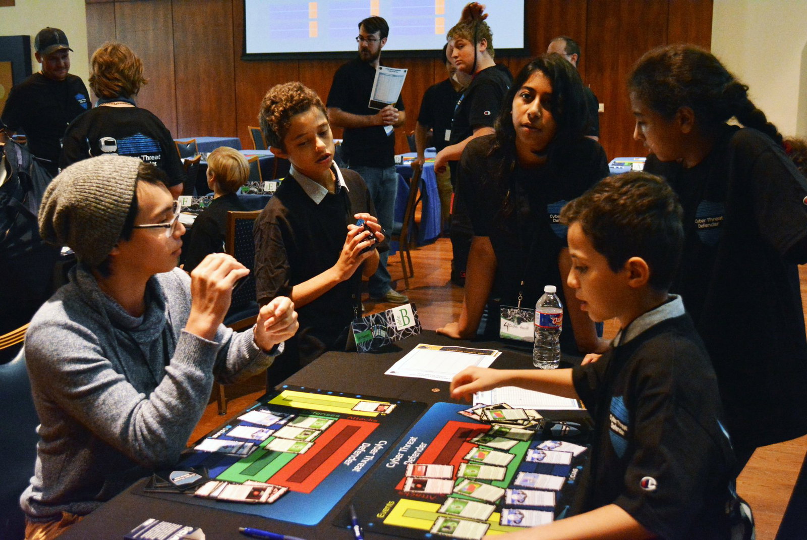 Several students stand around a table as two competitors finish their round of play