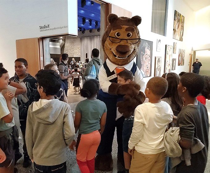 Alan CyBear hugging a student with other kids around him