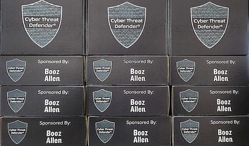 Stack of Cyber Threat Defender classroom boxes featuring logo of Booz Allen sponsor